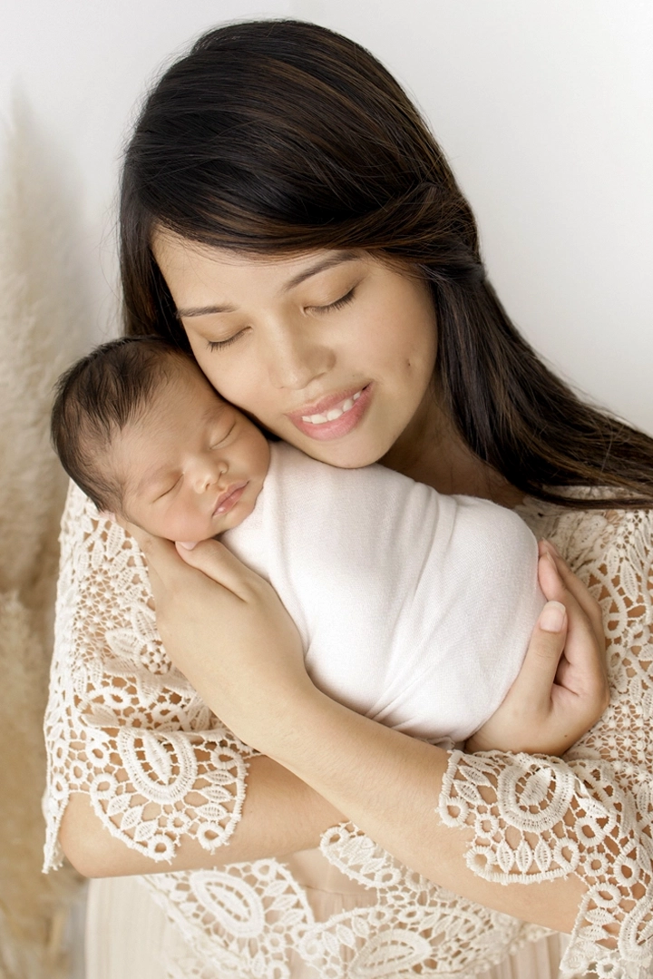 Photo d'une jolie maman qui tient son b&eacute;b&eacute; dans les bras tendrement lors d'un shooting photo